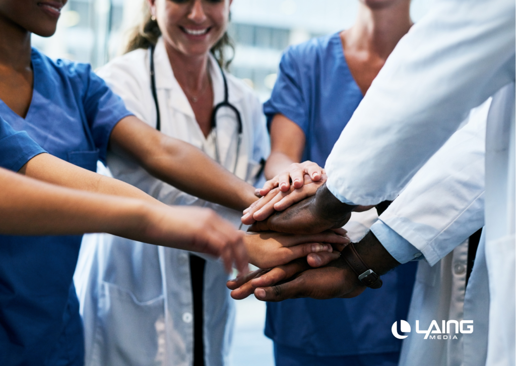 Group of healthcare professionals in a circle with their hands together with Laing Media white logo in bottom right corner.  
