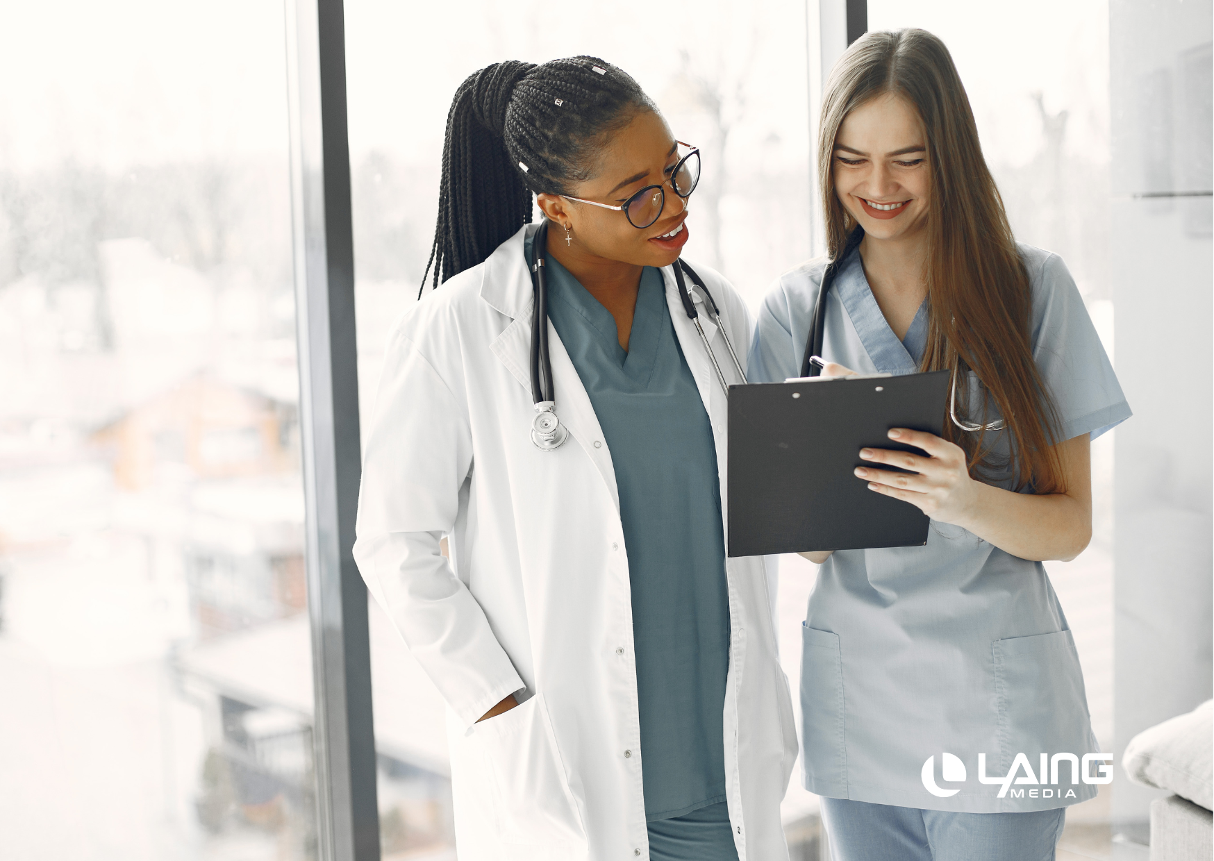 Two women in healthcare looking at a tablet with Laing Media logo on the bottom right corner.